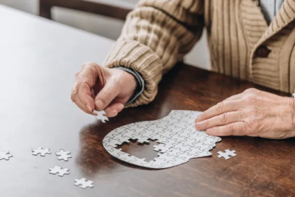 Iemand zit aan tafel en doet een puzzel in de vorm van hersenen